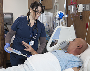 Healthcare provider caring for man in intensive care unit bed.