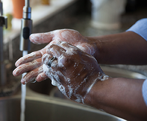 Primer plano de manos en el lavabo mientras corre el agua. Las manos están cubiertas con espuma de jabón.